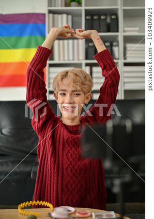 A confident Asian gay beauty influencer is recording his makeup video at home. A confident Asian gay beauty influencer is recording his makeup video at home. 103409923