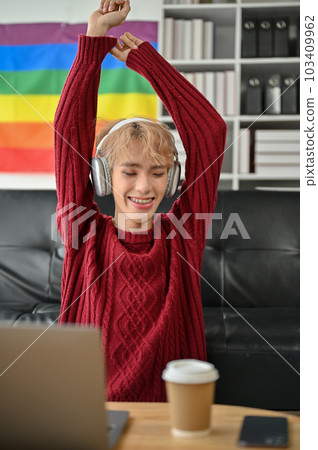 A joyful young Asian gay man is enjoying the music and dancing while sitting on a sofa A joyful young Asian gay man is enjoying the music and dancing while sitting on a sofa 103409962