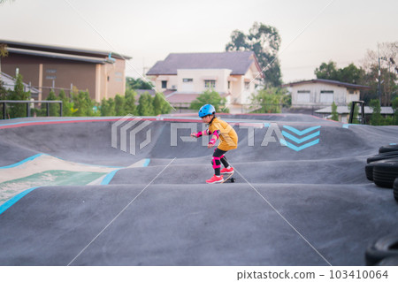 Child or kid girl playing surfskate or skateboard in skating rink or sports park at parking to wearing safety helmet elbow pads wrist and knee support Child or kid girl playing surfskate or skateboard in skating rink or sports park at parking to wearing safety helmet elbow pads wrist and knee support 103410064