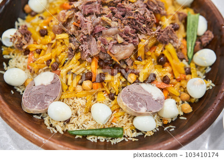 A traditional Uzbek dish called pilaf. Rice with meat, carrots, onions, quail eggs and kazy in a plate of astau on the table. A portion for three people. 103410174