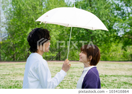 Couple standing with an umbrella in the park Couple standing with an umbrella in the park 103410864