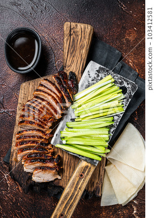 Sliced Peking Duck served with cucumber, green onion, and wheaten chinese pancakes on a meat cleaver. Dark background. Top view 103412581
