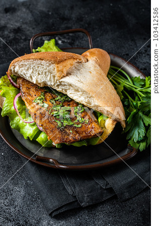 Sandwich balik Ekmek with grilled fillet of mackerel fish, tomatoes, onions and lettuce. Black background. Top view Sandwich balik Ekmek with grilled fillet of mackerel fish, tomatoes, onions and lettuce. Black background. Top view 103412586