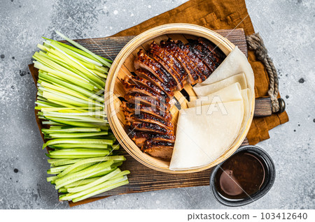 Peking Duck in bamboo steamer served with cucumber, green onion, and wheaten chinese pancakes and sauce Hoysin. Gray background. Top view Peking Duck in bamboo steamer served with cucumber, green onion, and wheaten chinese pancakes and sauce Hoysin. Gray background. Top view 103412640