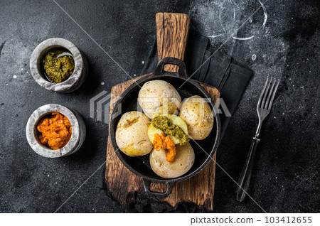 Papas arrugadas Canary islands wrinkled potatoes with green and red sauces served in a skillet. Black background. Top view 103412655