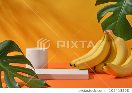 Fresh bunch of banana, jungle monstera leaves and cylinder white podium decorated on a yellow background with natural shadow leaves. Space for display cosmetic of banana extract Fresh bunch of banana, jungle monstera leaves and cylinder white podium decorated on a yellow background with natural shadow leaves. Space for display cosmetic of banana extract 103413368