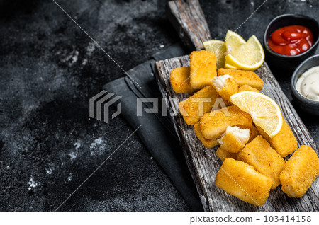 Golden roast Fish Sticks Fingers with sauce on a wooden board. Black background. Top view. Copy space Golden roast Fish Sticks Fingers with sauce on a wooden board. Black background. Top view. Copy space 103414158