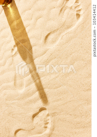 Shadow of beer bottle on warm sand. Textured image with footprints on sand. Beach chill on warm summer day with cool drink, refreshment Shadow of beer bottle on warm sand. Textured image with footprints on sand. Beach chill on warm summer day with cool drink, refreshment 103414412