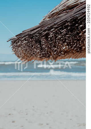 Straw beach rattan parasol at the empty beach with blue sky backgrounds sea ocean coast. Relaxing day. Copy space for your text. Idyllic travel and summer vacation concept. Straw umbrella 103414492