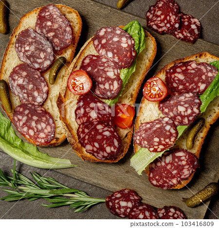 Toast with dried sausage lettuce on a dark wooden background, rustic style. 103416809