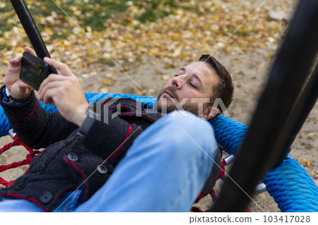 Man using smartphone while resting on swing outdoors Man using smartphone while resting on swing outdoors 103417028