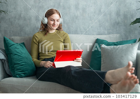 Headphones and woman on sofa and smart tablet, happy energy and mental health music in her home. Young person on couch listening to audio tech, electronics and podcast on computer in living room 103417129