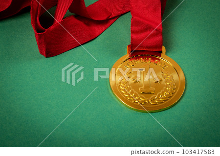 Gold medal with a red ribbon on a green background. Copy space. Close up 103417583