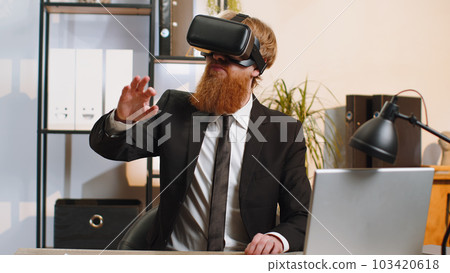 Young business man in VR goggles watch virtual reality video, working on simulation game at office Young business man in VR goggles watch virtual reality video, working on simulation game at office 103420618