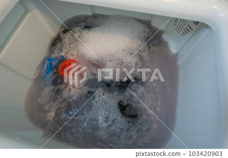 Dirty clothes in top loading washing machine. Clothes with bubble of laundry detergent in washing machine. Laundry concept. Top load washer. Housework. Washing machine and dirty water from cleaning. 103420903