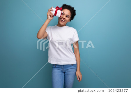 young brunette woman with afro hair holding a gift with a ribbon on a blue background with copy young brunette woman with afro hair holding a gift with a ribbon on a blue background with copy 103423277