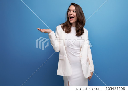 pleasant brunette woman in a dress shows her hand to the side on a studio background 103423308
