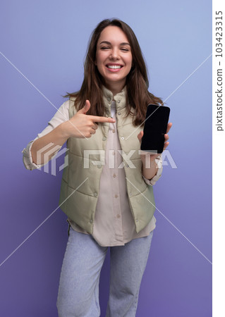 positive brunette young lady in casual style showing smartphone screen 103423315