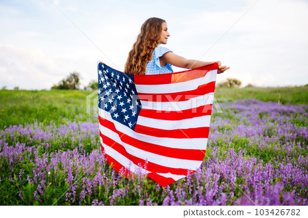 Young woman with american USA flag on blooming meadow. Independence Day, 4th July. Young woman with american USA flag on blooming meadow. Independence Day, 4th July. 103426782