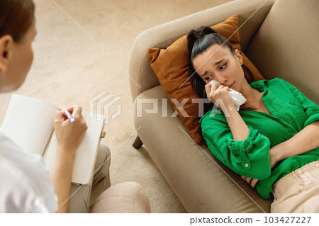 Top view of therapist making notes while female patient is lying on the couch and talking about her problems. 103427227