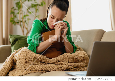 Young woman crying on couch in front of laptop. 103427729