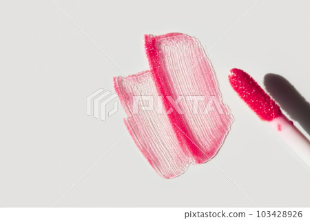 Smears of shining lip gloss and lip gloss brush on white background, hard shadows 103428926