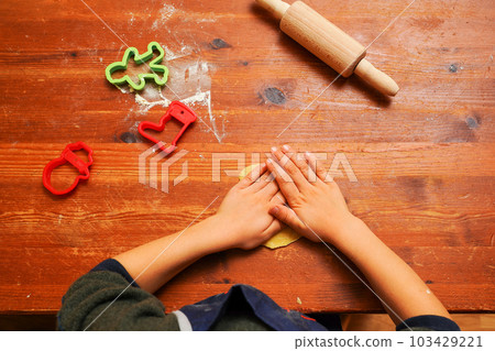 Hands of a toddler child cutting shaped biscuits out of dough on a brown wooden tabel. Christmas baking 103429221