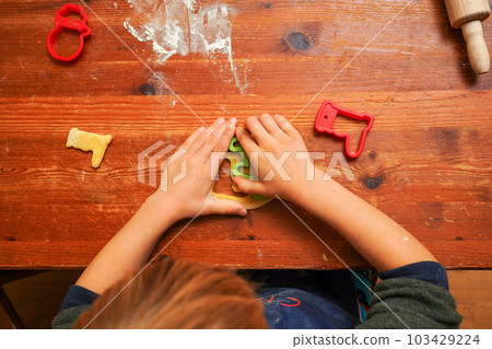 Hands of a toddler child cutting shaped biscuits out of dough on a brown wooden tabel. Christmas baking 103429224