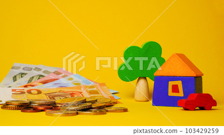 Euro cash money euro coins and banknotes with wood toy house, tree and auto on yellow background. Property Ownership Concept Euro cash money euro coins and banknotes with wood toy house, tree and auto on yellow background. Property Ownership Concept 103429259
