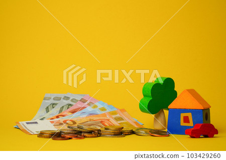 Euro cash money euro coins and banknotes with wood toy house, tree and auto on yellow background. Property Ownership Concept Euro cash money euro coins and banknotes with wood toy house, tree and auto on yellow background. Property Ownership Concept 103429260