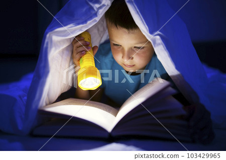 A young boy reading a book under the covers with a flashlight at dark night time A young boy reading a book under the covers with a flashlight at dark night time 103429965