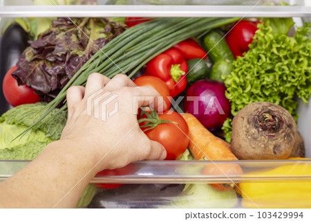 Mans hand is opening drawer of refrigerator with vegetables. Mans hand is opening drawer of refrigerator with vegetables. 103429994