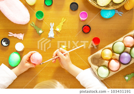 Child hands painting eggs for Easter on the wooden table at home. Preparation for Easter. 103431191