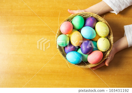 A girl, five years old, holding a basket with many colored Easter eggs in her hands. 103431192