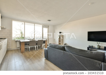 a living room and kitchen area in a modern apartment with wood flooring, white walls and light gray couches 103431510