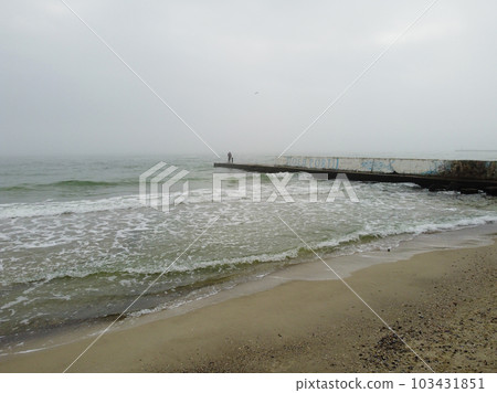 A Black see coast during a low tide and two people standing on a pier. 103431851