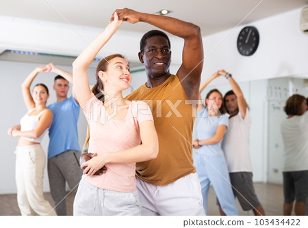 Joyful active adult men and women learning to dance in pairs in modern choreographic studio, indoors Joyful active adult men and women learning to dance in pairs in modern choreographic studio, indoors 103434422