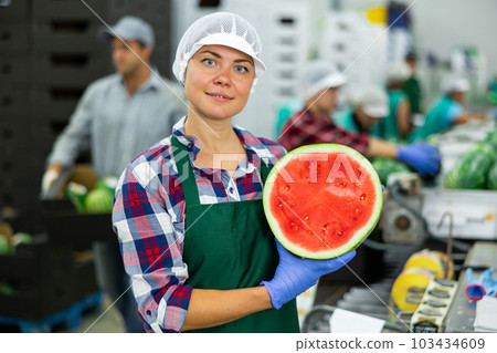 Smiling workwoman standing in fruit sorting factory with half of watermelon 103434609