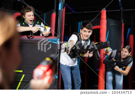 Laughing players mens and womens playing in teams in dark laser tag station Laughing players mens and womens playing in teams in dark laser tag station 103434753