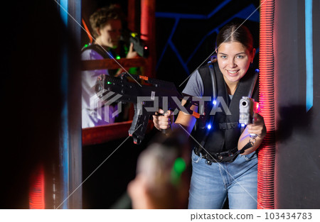 Smiling girl with laser pistol during playing laser tag with her friends in room Smiling girl with laser pistol during playing laser tag with her friends in room 103434783