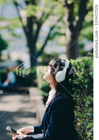 A high school girl sitting on a bench and listening to music 103437026