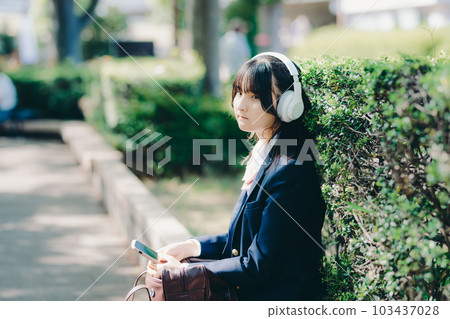 A high school girl sitting on a bench and listening to music 103437028