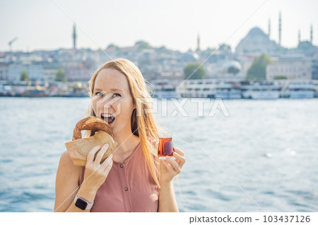 Woman in Istanbul having breakfast with Simit and a glass of Turkish tea. Glass of Turkish tea and bagel Simit against golden horn bay in Istanbul, Turkey. Turkiye Woman in Istanbul having breakfast with Simit and a glass of Turkish tea. Glass of Turkish tea and bagel Simit against golden horn bay in Istanbul, Turkey. Turkiye 103437126