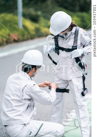 Site supervisor attaching a safety belt to a newcomer at a construction site Site supervisor attaching a safety belt to a newcomer at a construction site 103437801