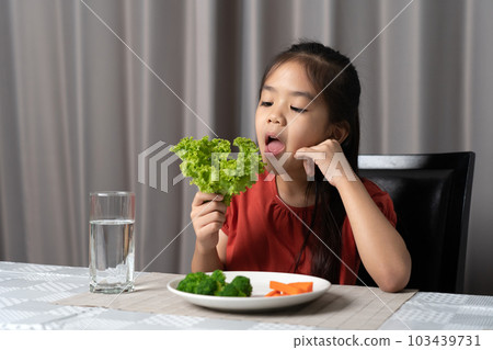 Asian little girl eating healthy vegetables with relish. Asian little girl eating healthy vegetables with relish. 103439731