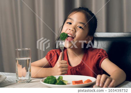 Asian little girl eating healthy vegetables with relish. Asian little girl eating healthy vegetables with relish. 103439732