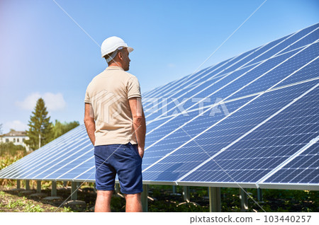 Back view of man in helmet next to solar system. Confident man looking at his investment. Male adult looking at photovoltaic batteries. Back view of man in helmet next to solar system. Confident man looking at his investment. Male adult looking at photovoltaic batteries. 103440257