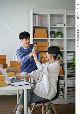 A cheerful Asian man, an online shop owner, is giving a high five to his girlfriend A cheerful Asian man, an online shop owner, is giving a high five to his girlfriend 103442601