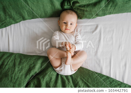 Portrait of a cute charming smiling laughing Caucasian white boy of six months old lying on a bed and looking at the camera. View from above. A happy lifestyle in childhood. 103442791