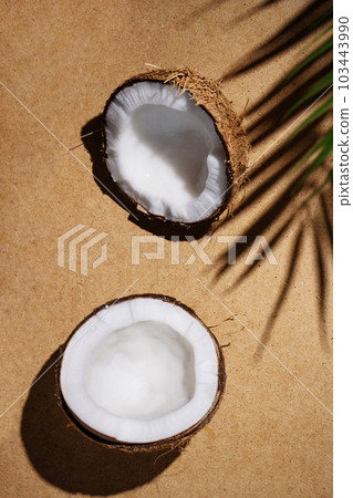 Summer tropical background with coconut and palm leaf shade. Cracked coconut and palm leaf on beige background. Summer wallpaper. Summer tropical background with coconut and palm leaf shade. Cracked coconut and palm leaf on beige background. Summer wallpaper. 103443990